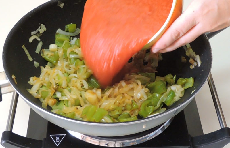 Añadiendo el tomate a la sartén con el pimiento, los ajos y la cebolla