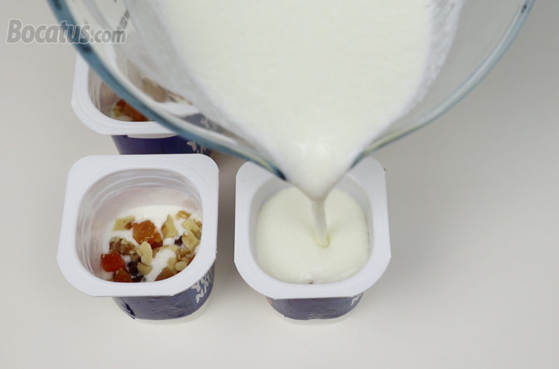 Repartiendo la crema de queso y los frutos secos en los envases de yogur